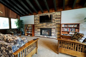 Ein gemütliches Wohnzimmer mit Kamin aus Stein, einem darüber angebrachten Flachbildfernseher und zwei hölzernen Bücherregalen voller Bücher.