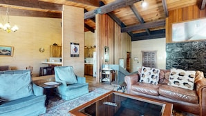 Un vaste espace de vie doté d’un plafond haut, de poutres en bois, d’un mur en pierre et d’un coin salon accueillant comprenant un canapé en cuir et des fauteuils.