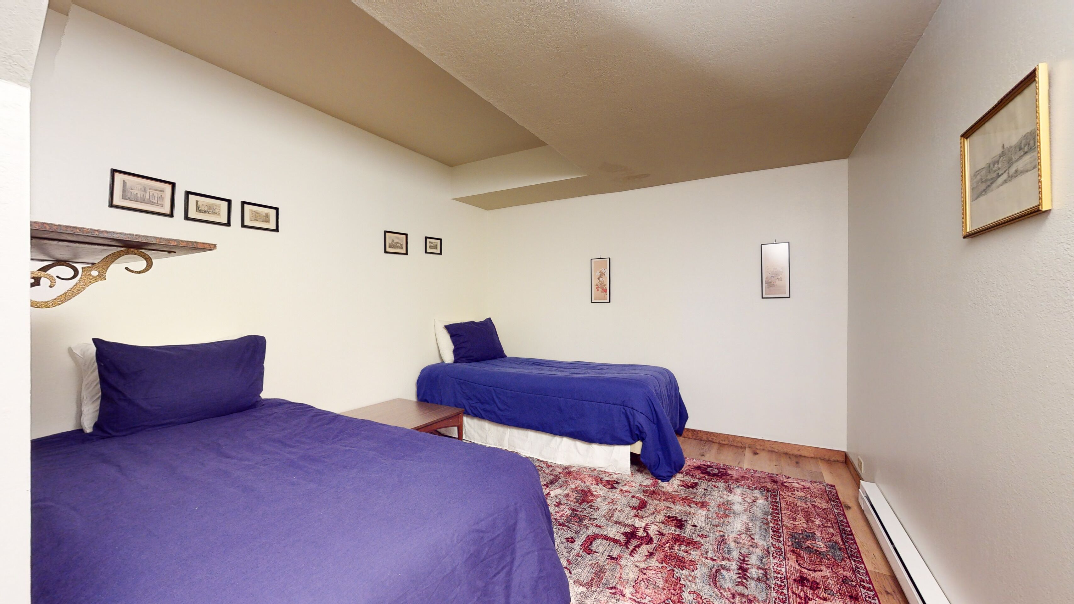 Une chambre avec deux lits, un tapis à motifs et plusieurs tableaux encadrés accrochés aux murs.