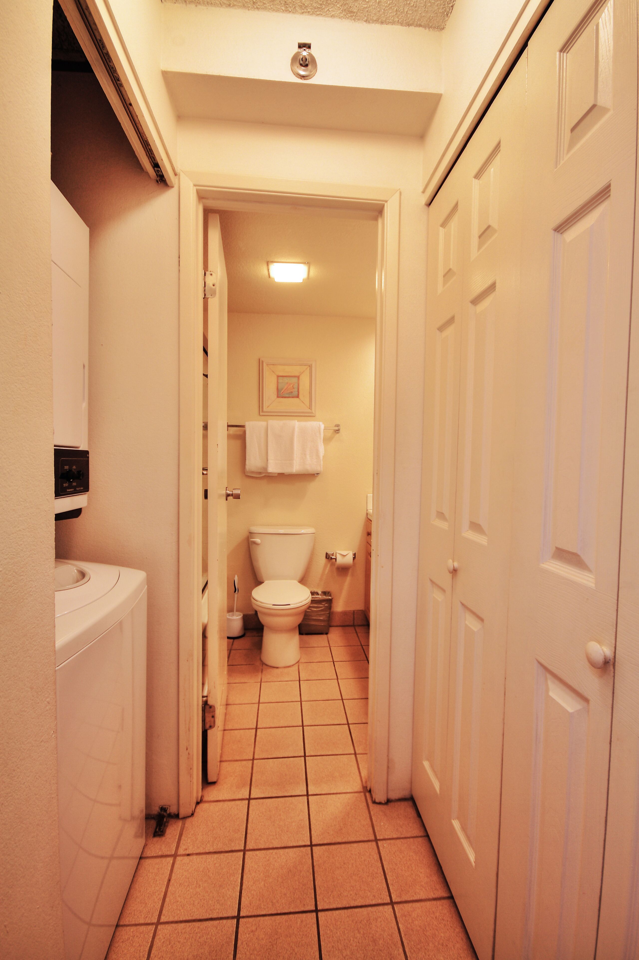 A narrow hallway with a toilet, a sink, and a door leading to another room.