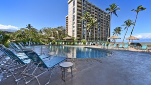 Ein Hotelpoolbereich mit Liegestühlen, einem kleinen Tisch und einem großen Gebäude im Hintergrund.