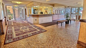 Eine Hotelhalle mit Empfangstresen, einem gemusterten Teppich, gefliestem Boden und Zimmerpflanzen.