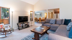 A living room with a TV, sofa, and coffee table. There is a dining area with chairs and a table in the background. - 47 McCloud | 3BR/3BA Incline Village, Hot Tub (Incline Village)