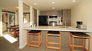 A modern kitchen with a central island, stainless steel appliances, and wooden stools. - Discovery 4 #135 1 Bedroom 1 Bath (Mammoth Lakes)