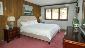 A bedroom with a large bed, wooden paneling on the walls, a painting, and a window with a view. - Mountainback #74 2 Bedroom 2 Bath (Mammoth Lakes)