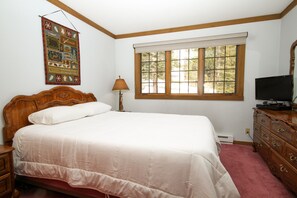 A bedroom with a large bed, a dresser, a television, a window with blinds, and a wall hanging. - Mountainback #74 2 Bedroom 2 Bath (Mammoth Lakes)