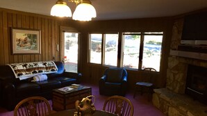 A cozy living room with a fireplace, a dining table with chairs, a blue armchair, and a couch with a blanket. - Mountainback #74 2 Bedroom 2 Bath (Mammoth Lakes)