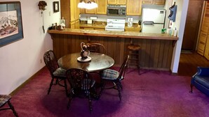 A compact kitchen with wooden cabinets, a central island, and a dining area with a round table and chairs. - Mountainback #74 2 Bedroom 2 Bath (Mammoth Lakes)