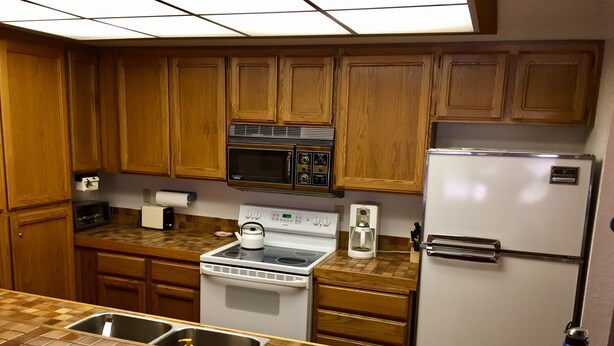 A kitchen with wooden cabinets, a microwave, a stove, a refrigerator, and a tiled countertop. - Mountainback #74 2 Bedroom 2 Bath (Mammoth Lakes)
