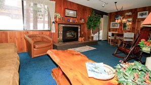 A cozy living room with a fireplace, wooden walls, a leather armchair, a wooden table, and a dining area with chairs. - Mammoth Ski & Racquet Club #25 (Mammoth Lakes)