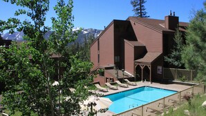 A pool area with a view of mountains, a wooden building, and a fenced deck. - Mammoth Ski & Racquet Club #25 (Mammoth Lakes)
