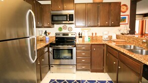 A kitchen with stainless steel appliances, wooden cabinets, a granite countertop, and a built-in oven. - Mammoth Ski & Racquet Club #25 (Mammoth Lakes)