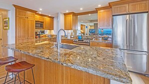 Eine Küche mit Granit Arbeitsplatten, Edelstahlgeräten, Holzschränken und einer großen Kochinsel mit Barhocker.