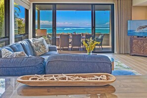A living room with a sofa, a dining table, and a view of the ocean. - Kahana Village #19 Beach Front Luxury (Lahaina)