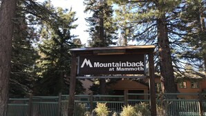 Een bord met de tekst 'Mountainback at Mammoth', met een stenen muur en bomen op de achtergrond.
