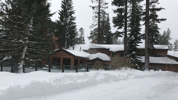 Een besneeuwde lodge met houten gevel, omringd door hoge sparren.