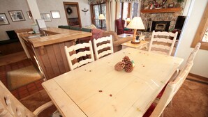 Een eethoek met een houten tafel en stoelen, een keukeneiland met een spoelbak, en een open haard op de achtergrond.