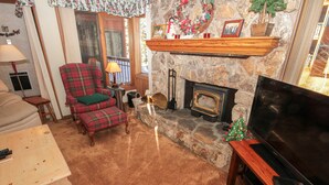 Een gezellige woonkamer met een stenen openhaard, een geruite fauteuil, een televisie en een kerstboom.