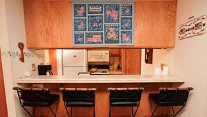 A kitchen with wooden cabinets, a white countertop, and a bar area with three black stools. - Discovery 4 #128, Loft - Pet Friendly (Mammoth Lakes)
