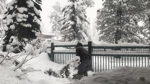 Eine Person in einer verschneiten Winterlandschaft mit einem Holzzaun und schneebedeckten Bäumen.