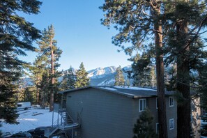 A cabin with a small deck, surrounded by tall pine trees and snow-covered ground, with mountains in the background. - Mountainback #53, Loft (Mammoth Lakes)