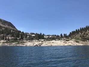 A rocky shoreline with a clear blue sky and a forested mountain in the background. - Mountainback #53, Loft (Mammoth Lakes)