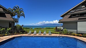 A swimming pool with lounge chairs, a view of the ocean, and a clear sky.