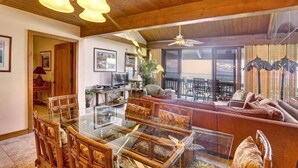 A spacious living area with a glass dining table, wooden chairs, a sofa, and a ceiling fan.