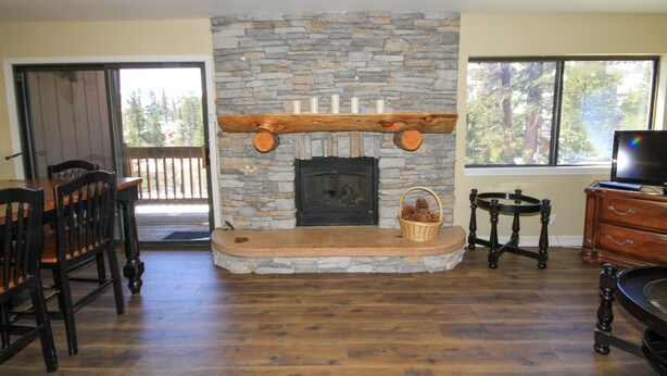 A stone fireplace with a wooden mantel, a dining area with wooden chairs, and a television on a wooden cabinet. - Mammoth Ski & Racquet Club #12 - Pet Friendly (Mammoth Lakes)