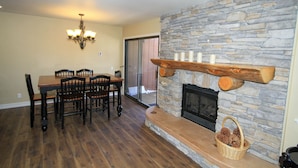 A dining area with a wooden table and chairs, a stone fireplace with a log shelf, and a chandelier. - Mammoth Ski & Racquet Club #12 - Pet Friendly (Mammoth Lakes)