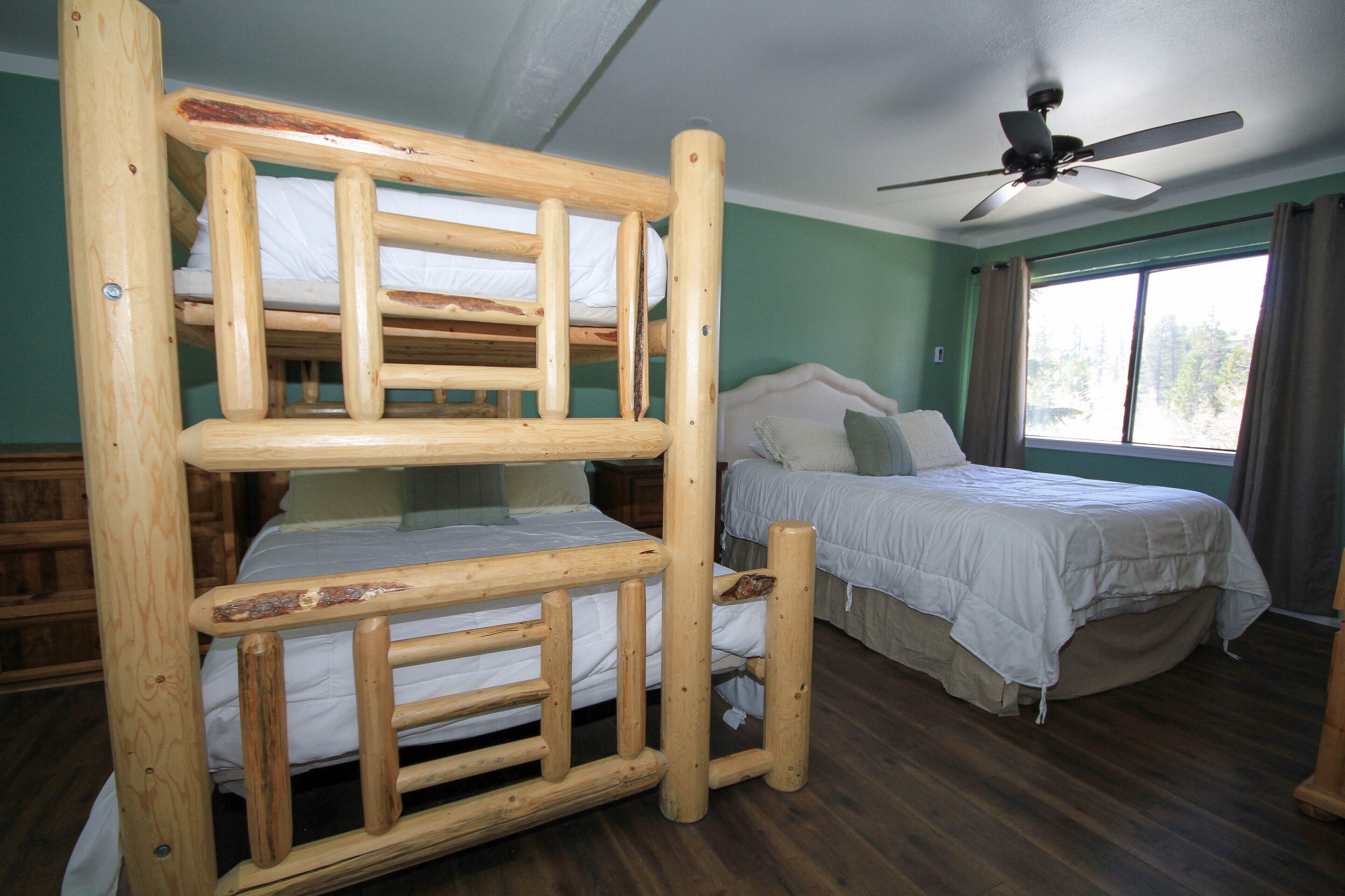 A room with a bunk bed, a single bed, a ceiling fan, and a window with curtains.