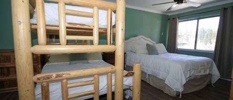 A room with a bunk bed, a single bed, a ceiling fan, and a window with curtains.