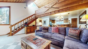 A cozy living room with a wooden staircase, a sofa with patterned cushions, a wooden coffee table, and a kitchen in the background. - Spacious Home, Private Laundry. Near Shops & Restaurants, Pool On-site (Mammoth Lakes)