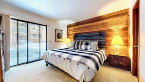 A bedroom with a large bed, wooden headboard, two bedside lamps, a nightstand, and a sliding glass door leading to a balcony. - Spacious Home, Private Laundry. Near Shops & Restaurants, Pool On-site (Mammoth Lakes)