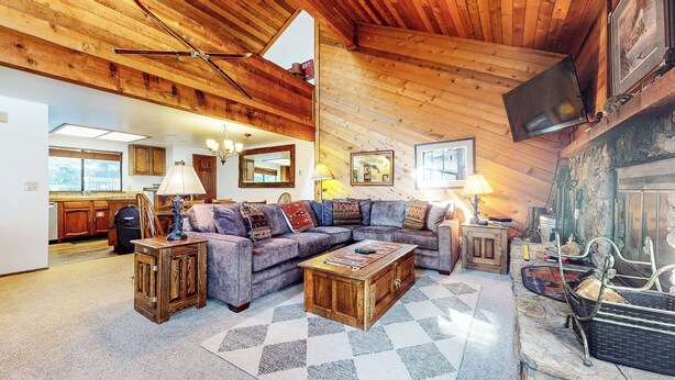 A cozy living room with a wooden ceiling, a large sectional sofa, a coffee table, and a television mounted on the wall. - Spacious Home, Private Laundry. Near Shops & Restaurants, Pool On-site (Mammoth Lakes)