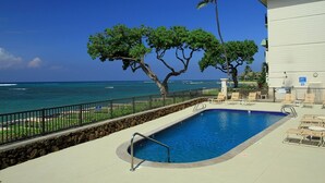 A swimming pool with a view of the ocean, surrounded by lounge chairs and a stone wall. - Vitamin Sea available on Maui Come Play at Kahana Reef 402   (Lahaina)