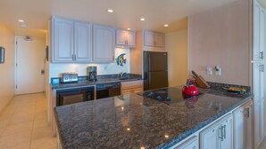 A modern kitchen with granite countertops, stainless steel appliances, and white cabinetry. - Vitamin Sea available on Maui Come Play at Kahana Reef 402   (Lahaina)