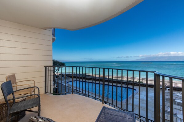 A balcony with a view of the ocean, a pool, and lounge chairs. - Direct Oceanfront • AC • Top Floor Views • Peaceful West Maui (Kahana)