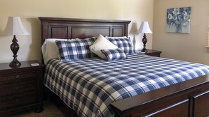 A neatly made bed with a plaid bedspread, two bedside tables with lamps, and a floral painting on the wall. - Mountainback #57, Den (Mammoth Lakes)