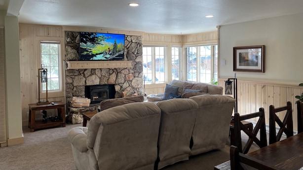 A cozy living room with a stone fireplace, a large flat-screen TV mounted above it, and a beige sectional sofa. - Mountainback #57, Den (Mammoth Lakes)