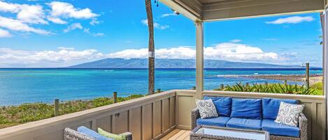 A covered outdoor seating area with wicker furniture and a view of the ocean.