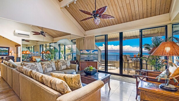 A spacious living area with a large sofa, a dining table, and a balcony with a view of the ocean. - Kahana Village #21 Beach Front Luxury (Lahaina)