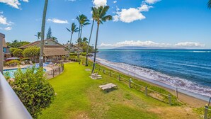 A beachfront property with a swimming pool, lounge chairs, and a view of the ocean. - Kahana Village #21 Beach Front Luxury (Lahaina)