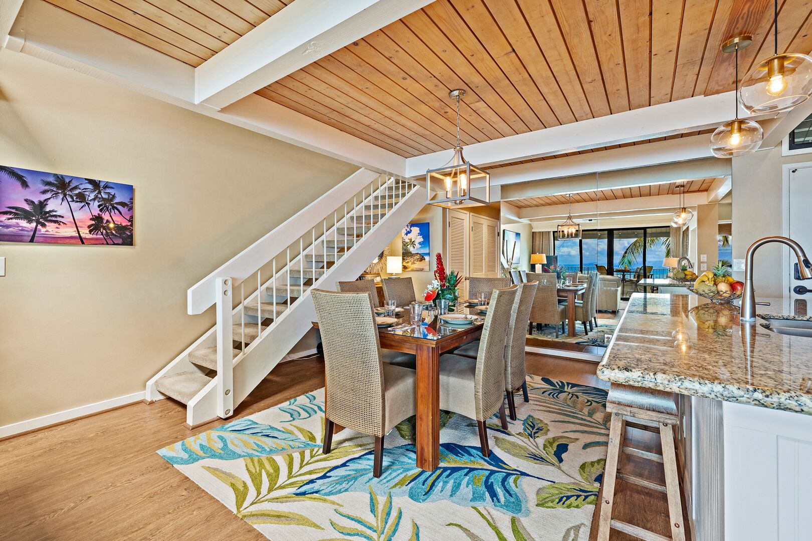 A spacious dining area with a high ceiling, a staircase, and a view of the ocean.
