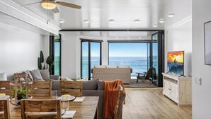 A modern living room with a dining area, large windows, and a ceiling fan. - Spacious Family Beachfront Getaway - 809-4 (Oceanside)