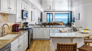 A modern kitchen with white cabinetry, granite countertops, and a view of the ocean through large windows. - Spacious Family Beachfront Getaway - 809-4 (Oceanside)