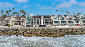 A beachfront hotel with multiple balconies, a rocky shoreline, and palm trees. - Spacious Family Beachfront Getaway - 809-4 (Oceanside)