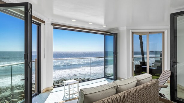 A balcony with a view of the ocean, a wicker sofa, and a glass door. - Spacious Family Beachfront Getaway - 809-4 (Oceanside)
