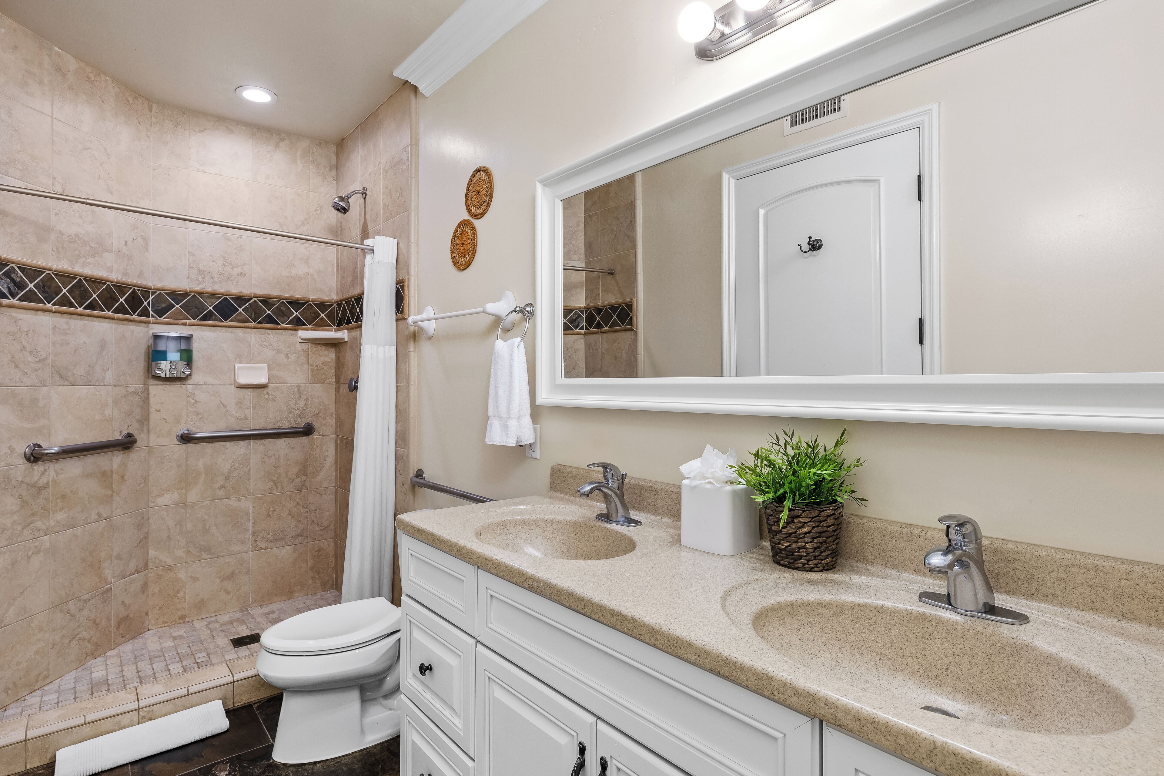 A bathroom with a shower, toilet, two sinks, and a large mirror.