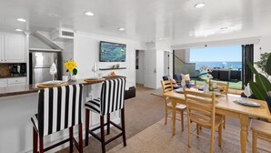 A modern kitchen with white cabinets, a stainless steel refrigerator, and a dining area with striped chairs and a wooden table. - Single Family Gorgeous Beachfront Mansion on the Sand P1733-0 (Oceanside)